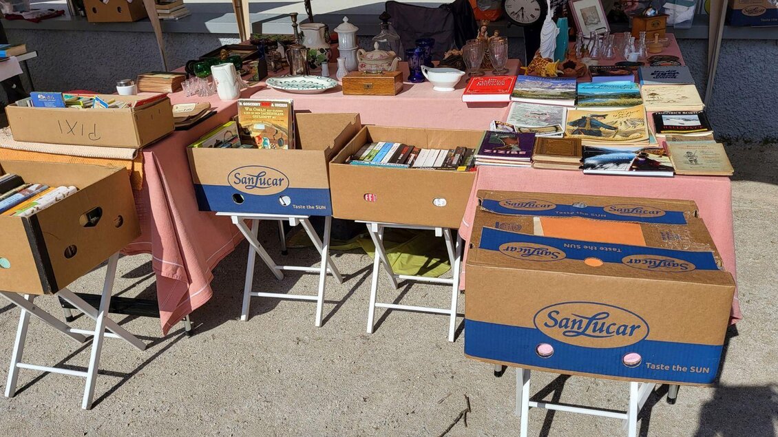 Ein Marktstand mit mehreren Kisten voller Bücher und verschiedenen kleinen Gegenständen. Auf dem Tisch sind weitere Artikel wie Geschirr und Dekorationen ausgestellt. | © Petra Kirchschlager