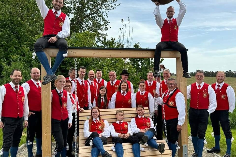 Eine große Blasmusikgruppe posiert auf einer Wiese vor einer Steinmauer. Alle Mitglieder tragen traditionelle Trachten und halten verschiedene Musikinstrumente. | © Trachtenkapelle Ebersdorf_Oststeiermark
