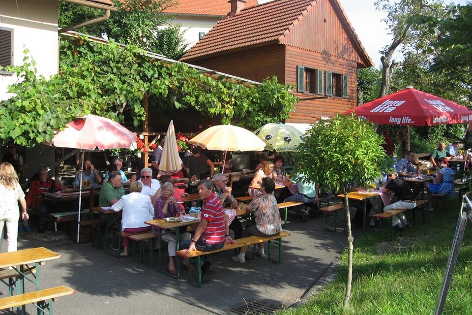 Ein fröhliches Restaurant im Freien mit vielen Gästen, die an Tischen sitzen. Bunte Schirme spenden Schatten unter der grünen Laube. | © Ga Weint Gehn Gemeinschaft
