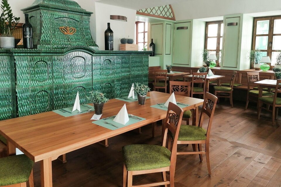 Ein gemütliches Restaurant mit Holztischen und Stühlen. Der grüne Kachelofen und die großen Fenster sorgen für eine einladende Atmosphäre. | © Hotel Erzherzog Johann
