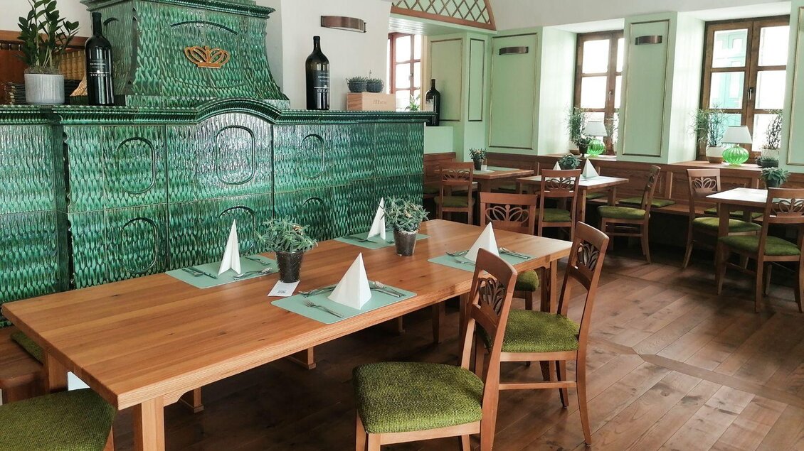 Ein gemütliches Restaurant mit Holztischen und Stühlen. Der grüne Kachelofen und die großen Fenster sorgen für eine einladende Atmosphäre. | © Hotel Erzherzog Johann