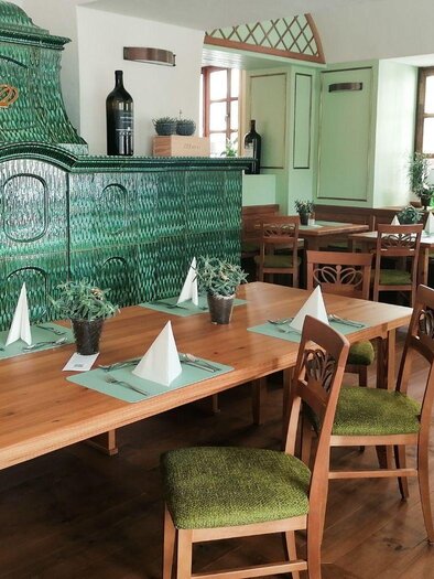 Ein gemütliches Restaurant mit Holztischen und Stühlen. Der grüne Kachelofen und die großen Fenster sorgen für eine einladende Atmosphäre. | © Hotel Erzherzog Johann