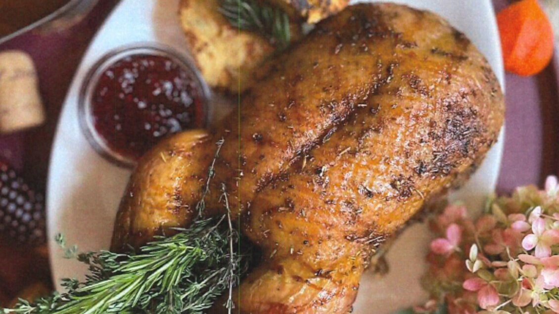 Ein lecker gegrilltes Huhn mit frischen Kräutern und einer Beilage. Daneben befinden sich eine Sauce und einige dekorative Blumen. | ©  Wirtshaus s'Johann, Bad Aussee