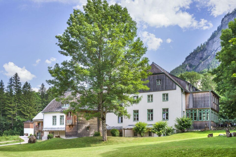 Ein schönes Gebäude umgeben von Bäumen und Wiesen. Im Hintergrund sind Berge zu sehen. | © JUFA Hotel Grundlsee