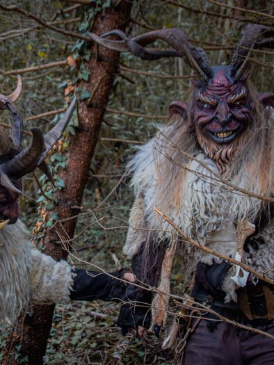 Zwei mystische Kreaturen mit Hörnern und pelzigen Kostümen stehen im Wald. Sie wirken geheimnisvoll und furchterregend zwischen den Bäumen. | © Übelbacher Gleinalm Pass