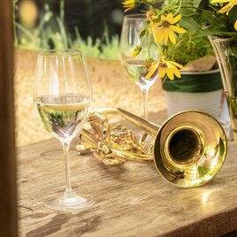 A trumpet with two wine glasses on a shiny wooden plate with a bouquet of autumn flowers beside it in the sunshine. | © Die Abbilderei