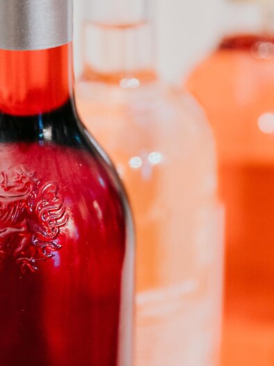 A selection of decorative wine bottles in various shades of rose. The bottle in the foreground is red and has an elegant closure. | © Wein Steiermark-Johanna Lamprecht