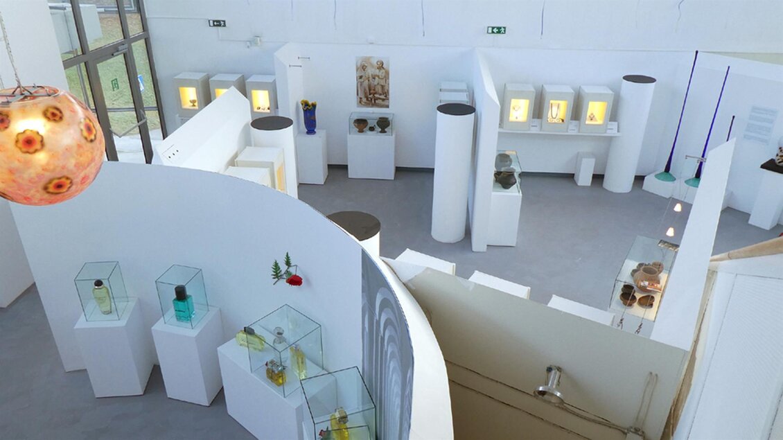 Ein modernes Ausstellungsraum mit weißen Wänden und Säulen. Vitrinen zeigen verschiedene Kunstobjekte und Skulpturen. | © Glasmuseum Bärnbach, Zvonka Pozun