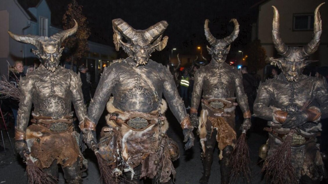 Gruppierte Menschen in beeindruckenden, dämonischen Kostümen mit Hörnern stehen in einer dunklen Straße. Die Atmosphäre ist festlich und geheimnisvoll. | © Wabi Gruam Teifln
