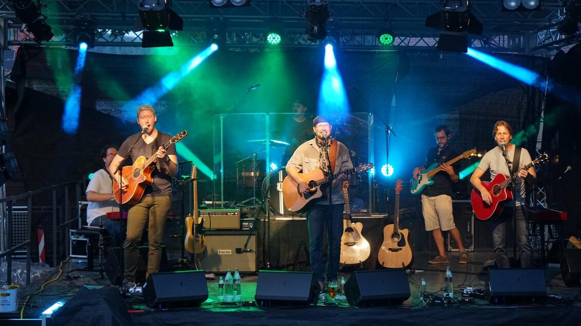 Eine Band spielt live auf einer Bühne mit bunten Lichtern. Es sind mehrere Musiker mit E-Gitarren zu sehen. | © Stadtgemeinde Köflach