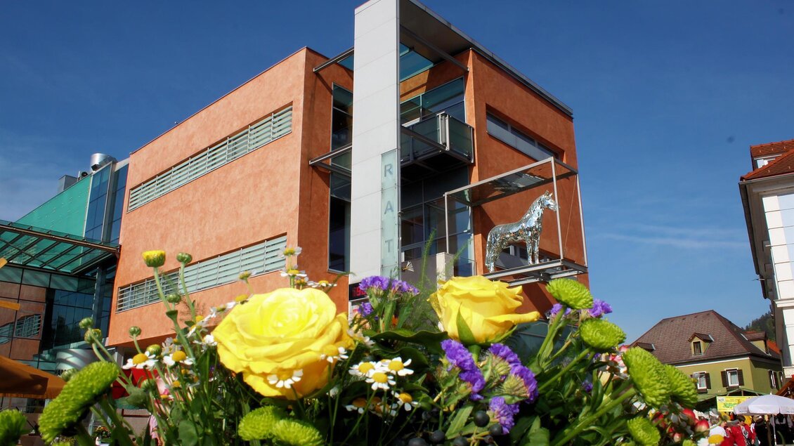 Ein modernes Gebäude mit Glas- und Stahlelementen, umgeben von bunten Blumen. Der Himmel ist klar und blau, was die lebendige Atmosphäre unterstreicht. | © Robert Cescutti