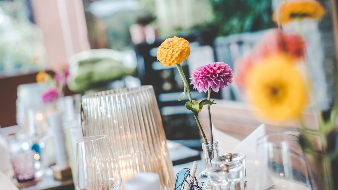 Ein schön gedeckter Tisch mit bunten Blumen in Vasen. Die Atmosphäre ist einladend und freundlich. | © Garten Hotel Ochensberger