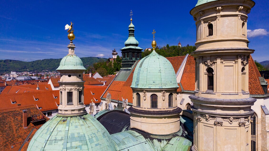 Eine beeindruckende Ansicht von historischen Gebäuden mit grünen Kuppeln und roten Dächern. Der klare blaue Himmel ergänzt die schöne Architektur der Stadt. | © Graz Tourismus - Harry Schiffer