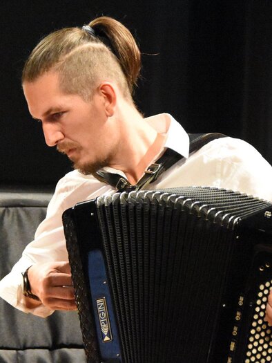 Bernd Kohlhofer plays accordion on a stage in front of a dark background. | © Krumusik