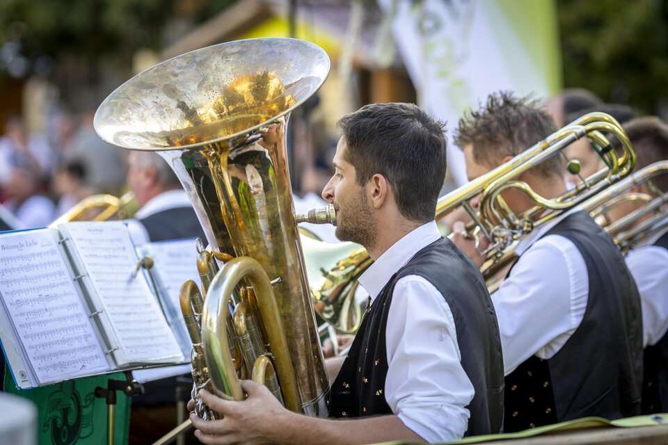 Musiker einer Blaskapelle spielen Tuba und Posaunen bei einem Konzert im Freien. Vor ihnen stehen Notenständer. | © Ivents Kulturagentur-Erwin Scheriau