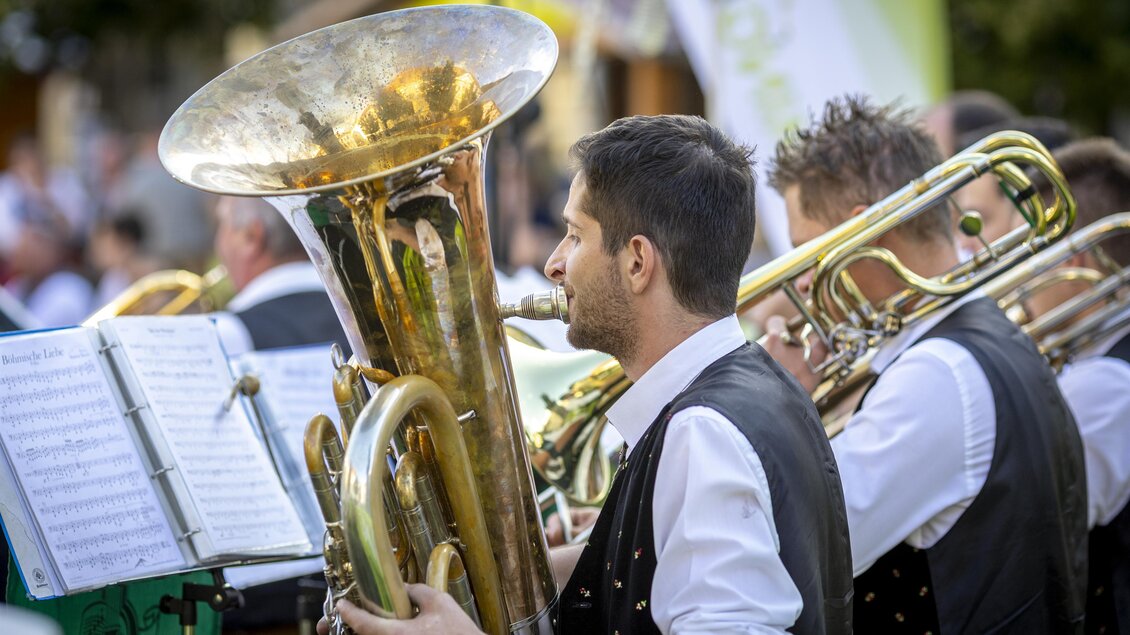 Musiker einer Blaskapelle spielen Tuba und Posaunen bei einem Konzert im Freien. Vor ihnen stehen Notenständer. | © Ivents Kulturagentur-Erwin Scheriau