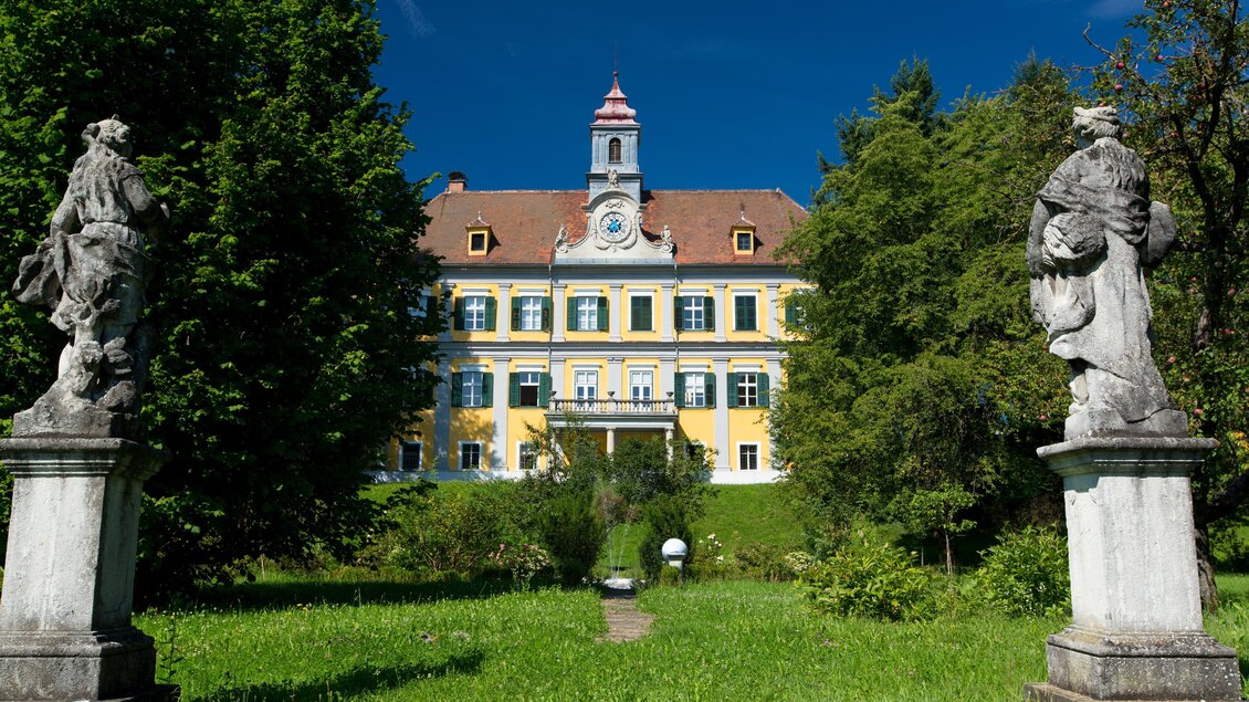 Gelbes Schloss in Premstätten mit Uhrturm, grünen Fensterläden und Garten, flankiert von zwei steinernen Statuen.  | © Region Graz-Harry Schiffer