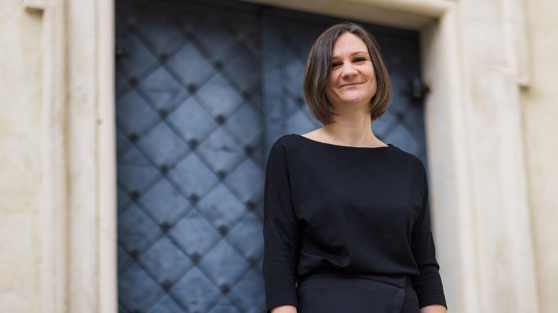 Porträt der Dirigentin Melissa Dermastia in schwarzer Kleidung vor einer dunklen, gemusterten Tür. | © Gerd Neuhold