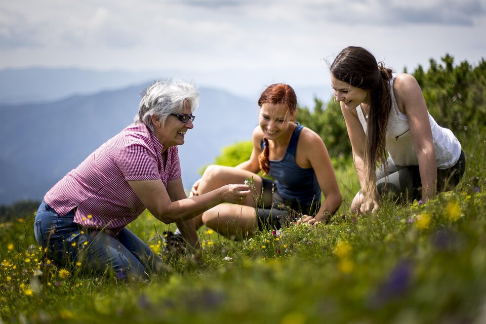 Drei Frauen sitzen auf einer Wiese in den Bergen und betrachten Pflanzen. Sie lachen und genießen die Natur. | © TV Hochsteiermark, Tom Lamm