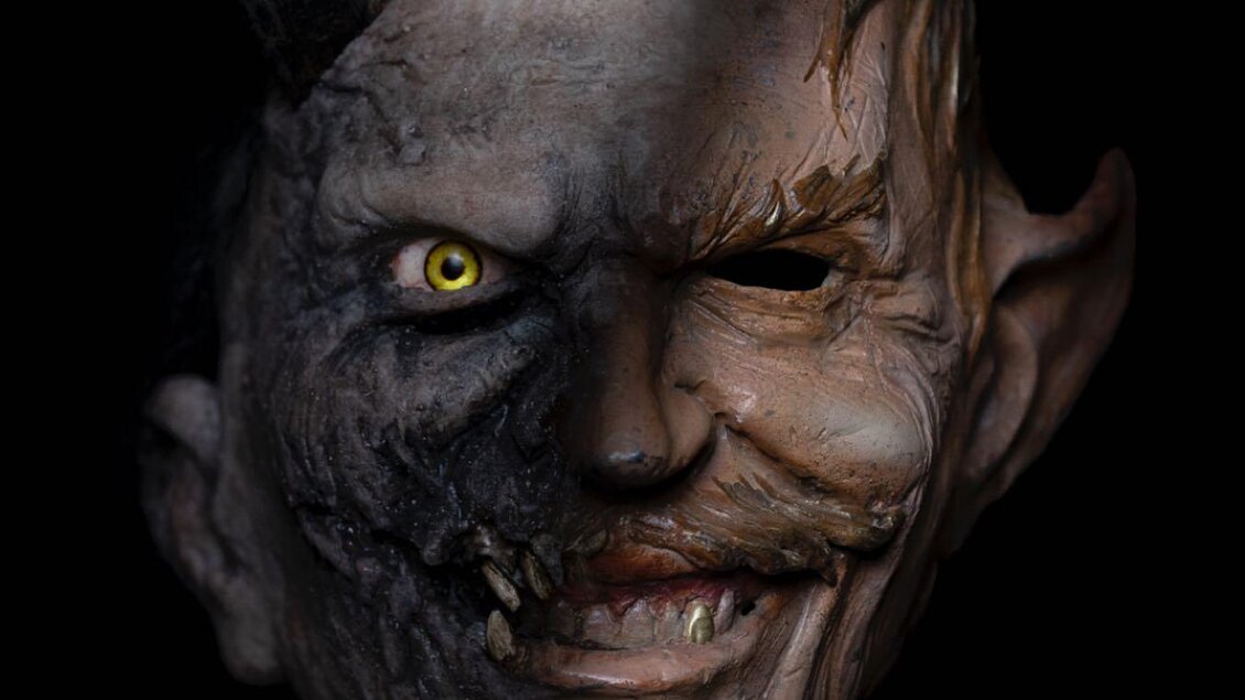 Eine maske mit einem gespaltenen Gesicht, eine Seite ist dämonisch und furchterregend, die andere Seite wirkt menschlich und grinsend. Sie hat Hörner und leuchtende Augen. | © Kuim Teifl / Schwoazmoar Bartl