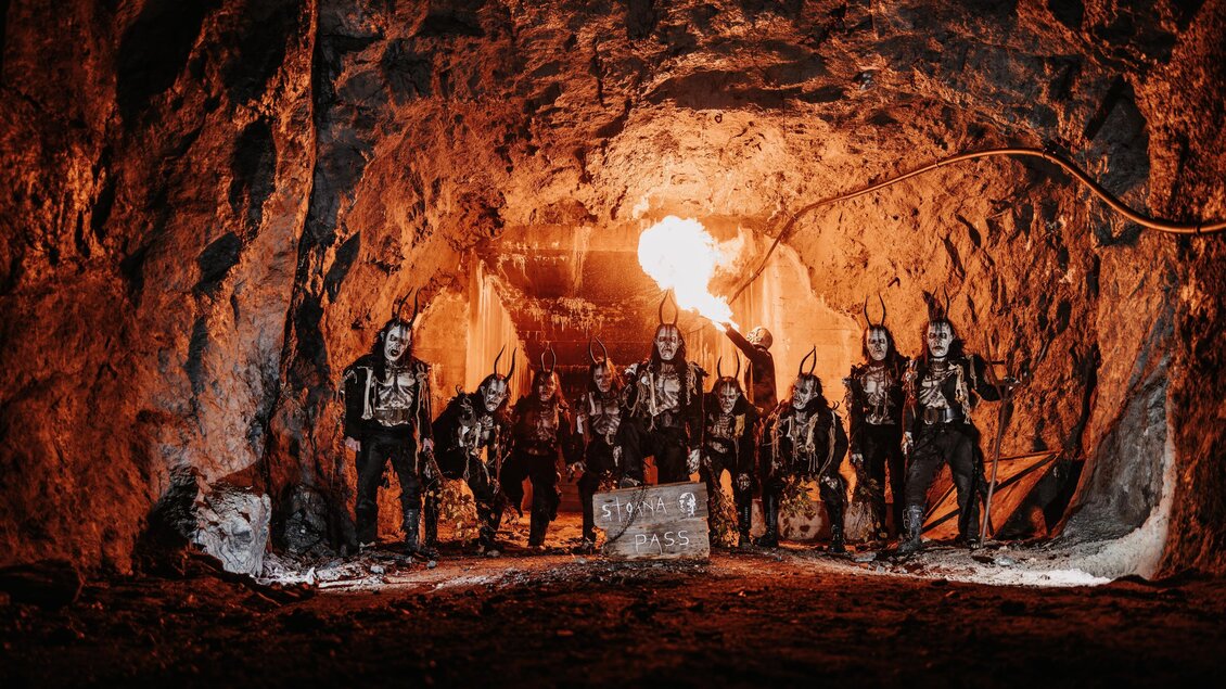 Eine Gruppe von Menschen steht in einer dunklen Höhle, umgeben von Felsen. Sie tragen auffällige Kostüme und schminken ihre Gesichter. | © Stoana Pass