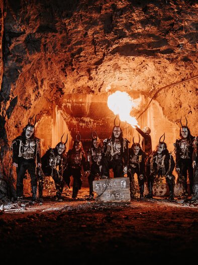 Eine Gruppe von Menschen steht in einer dunklen Höhle, umgeben von Felsen. Sie tragen auffällige Kostüme und schminken ihre Gesichter. | © Stoana Pass