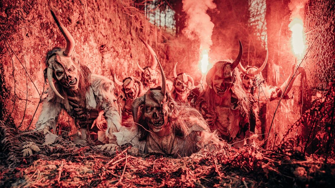 Eine Gruppe von Wesen mit Hörnern und gruseligen Masken in einem dunklen, nebligen Wald. Roter Rauch und ein unheimliches Licht verstärken die düstere Atmosphäre. | © Stoana Pass