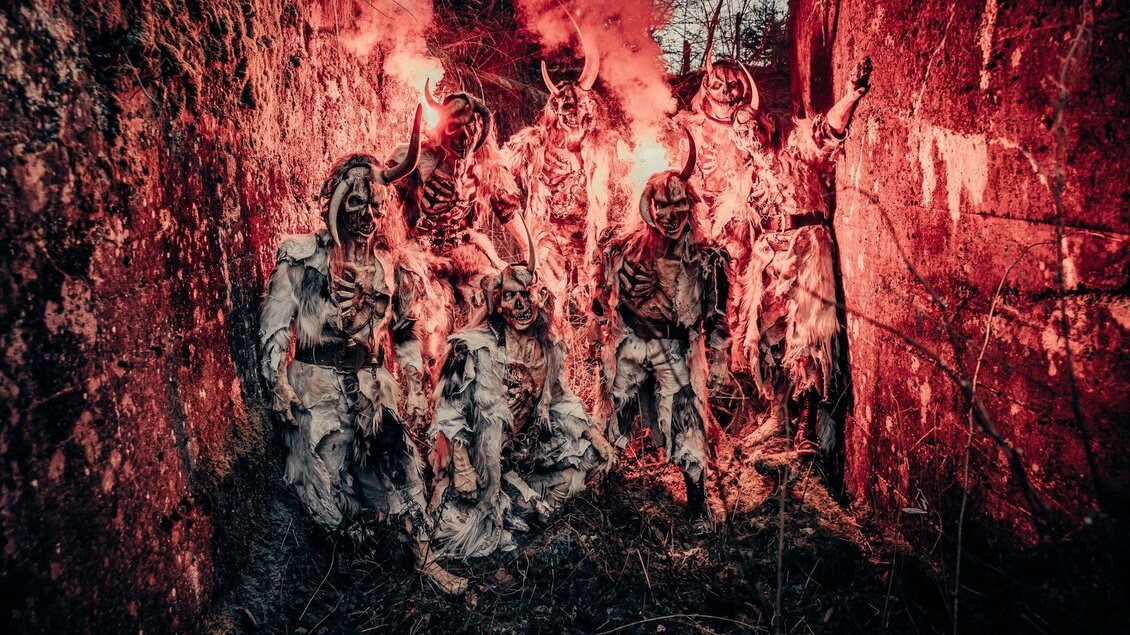 Eine Gruppe von mythologischen Wesen in gruseligen Kostümen steht in einer dunklen Umgebung. Rote Rauchfackeln erzeugen eine unheimliche Atmosphäre. | © Stoana Pass