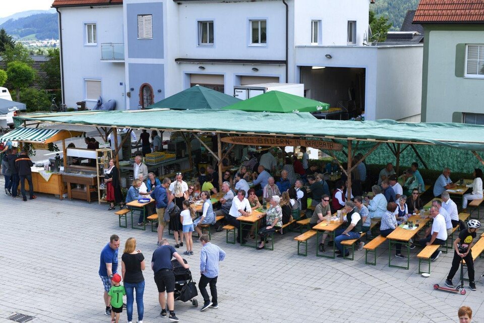 Eine belebte Freiluftveranstaltung mit vielen Tischen und Gästen unter grünen Sonnenschirmen. Im Hintergrund sind Häuser und ein klarer Himmel zu sehen. | © Marktgmeinde Kraubath