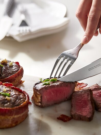 A juicy piece of meat is being sliced on a cutting board. In the background, a glass of wine and dishes can be seen. | © Weber Grill