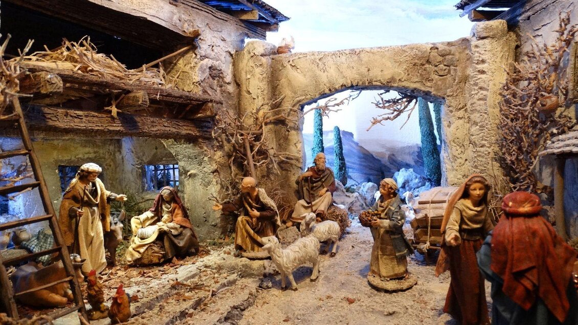 Eine traditionelle Krippe mit mehreren Figuren, die das Leben in einem Dorf darstellen. Im Hintergrund sind Berge und eine Straße zu sehen. | © Elisabeth Schupfer