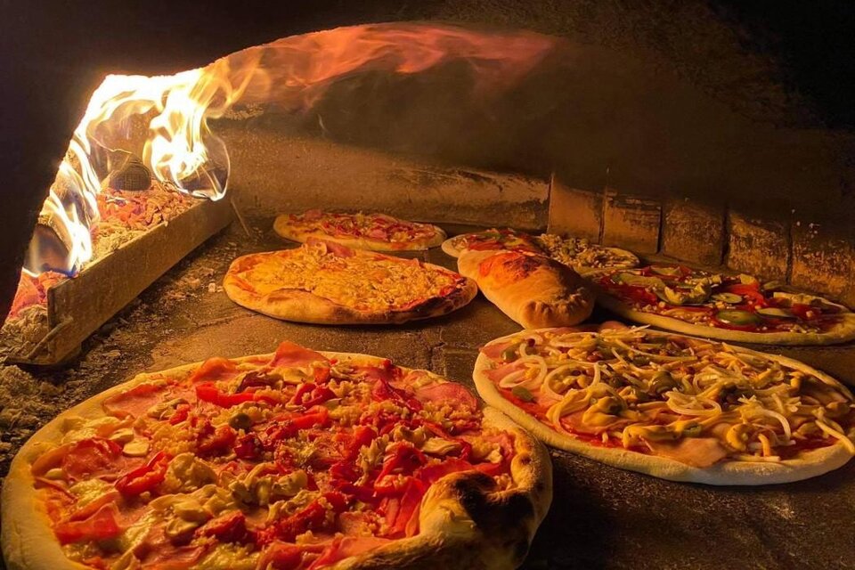 Mehrere belegte Pizzen backen neben offenem Feuer in einem traditionellen Holzofen. | © pizzerija-pod-gradom