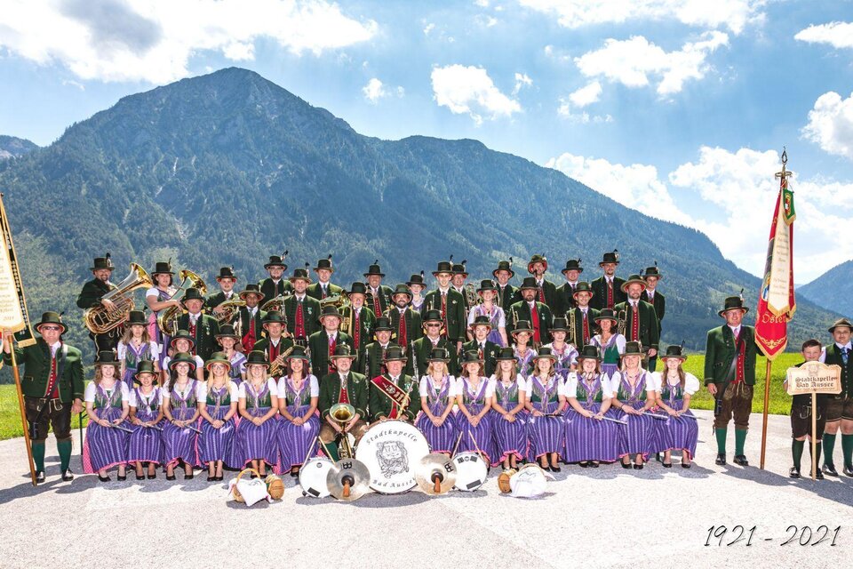 Die Stadtmusikkapelle Bad Aussee ist eine festliche, große Musikgruppe in Tracht. Im Hintergrund ist die Ausseerland Berglandschaft unter einem klaren Himmel zu sehen.</p> | © Erich Kainzinger