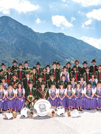 The city band Bad Aussee is a festive, large music group in traditional clothing. In the background, the Ausseerland mountain landscape can be seen under a clear sky.</p> | © Erich Kainzinger