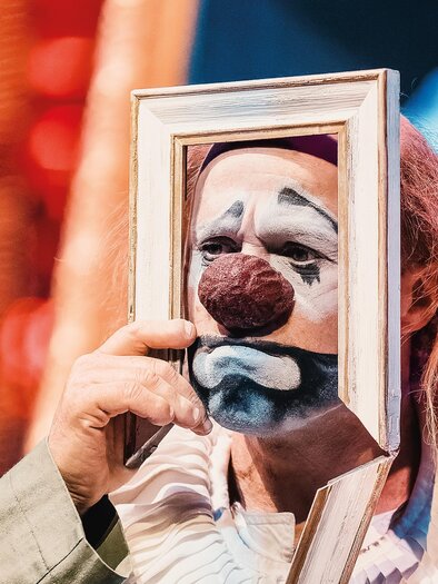 Clown with a white-painted face holds a picture frame in front of his face during a La Strada performance in Kalsdorf. | © Jolanda Hofmann