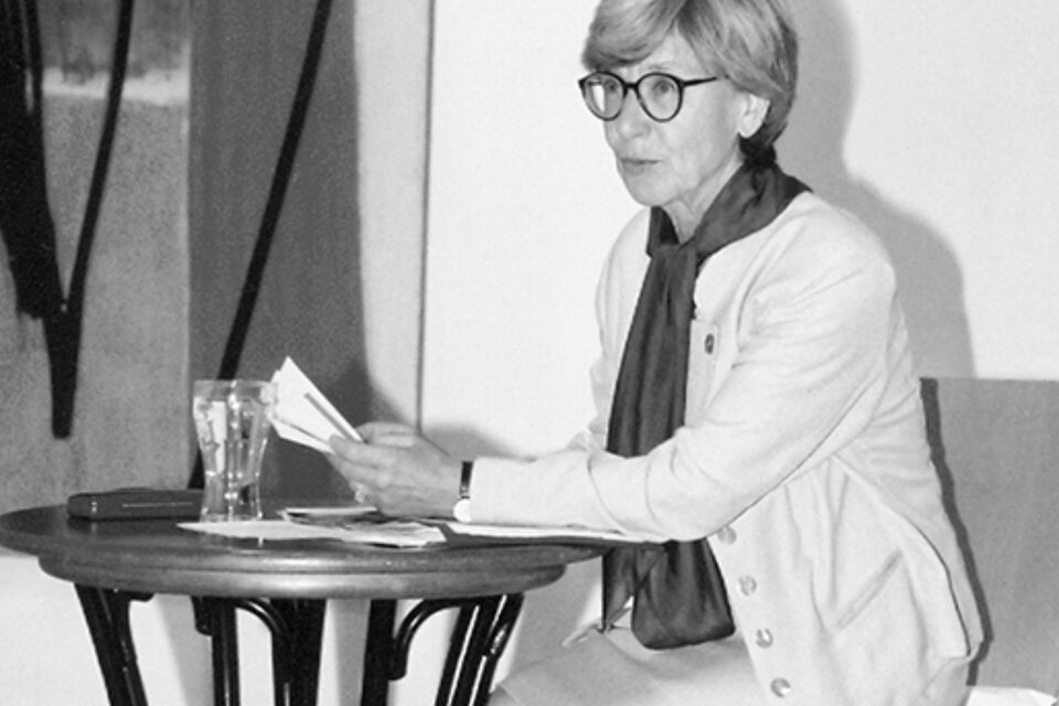 Hedwig Wingler liest bei einer Veranstaltung im Kunsthaus Köflach aus einem Buch und sitzt dabei an einem Tisch vor einer Präsentationsfläche. | © agathon koren