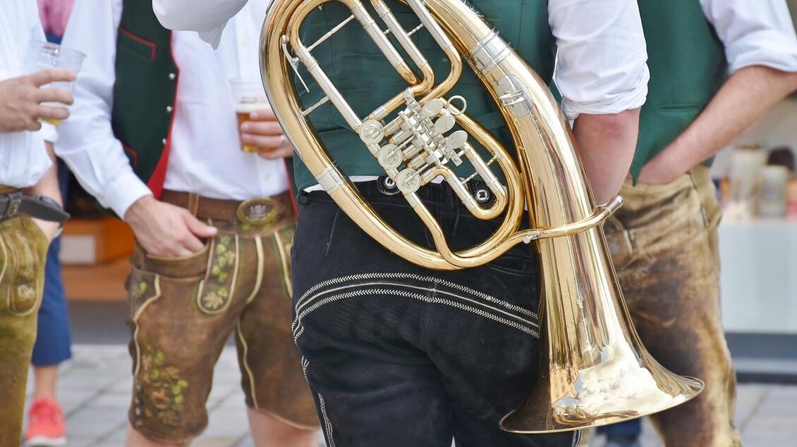 Eine Person mit einem Euphonium steht in einer Gruppe, die traditionelle Kleidung trägt. Im Hintergrund sind Biergläser und weitere Personen zu sehen. | © pixabay.com