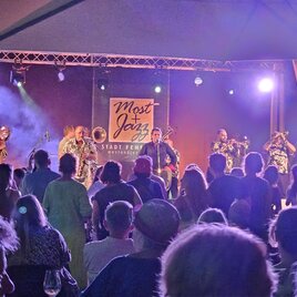 Ein buntes Konzert mit einer Jazzband auf der Bühne. Die Zuschauer genießen die Musik unter buntem Licht. | © Sebastian Friedl