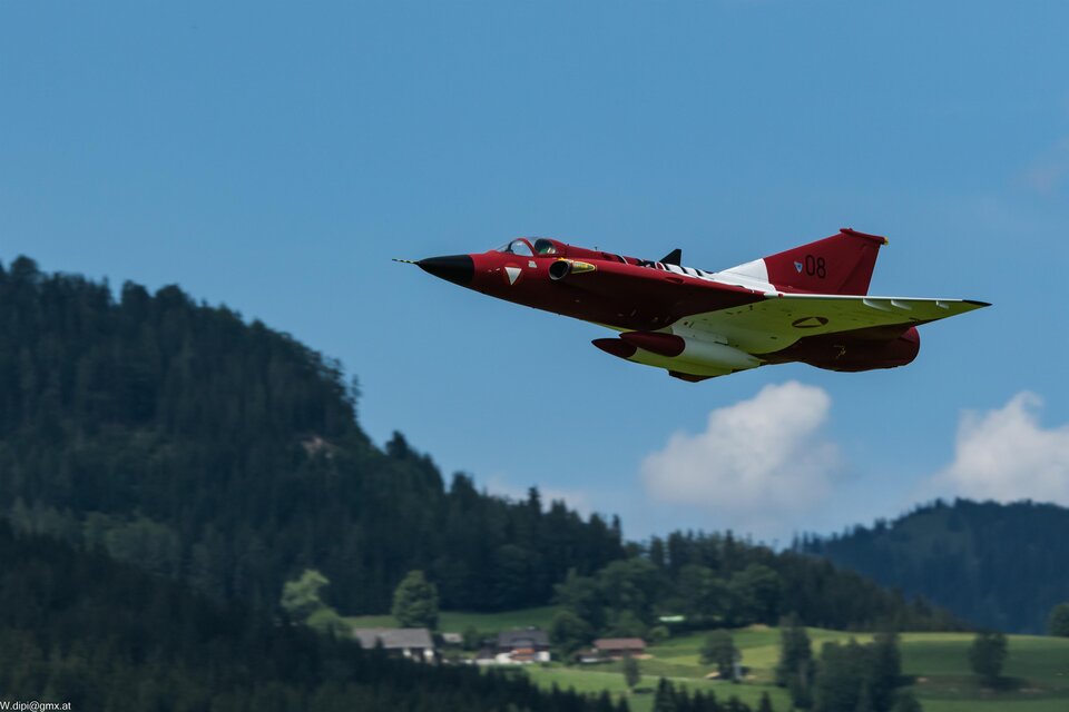 Das Bild zeigt einen fliegenden rot-weissen Jet, im Hintergrund sieht man blauen Himmel, Wald und einige Häuser | © FCS Turnau