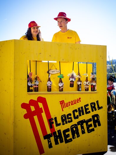 Ein farbenfrohes Theater mit dem Namen "Flascherl Theater". Zwei Personen stehen hinter der Theke und präsentieren verschiedene Getränke. | © Tv Murau