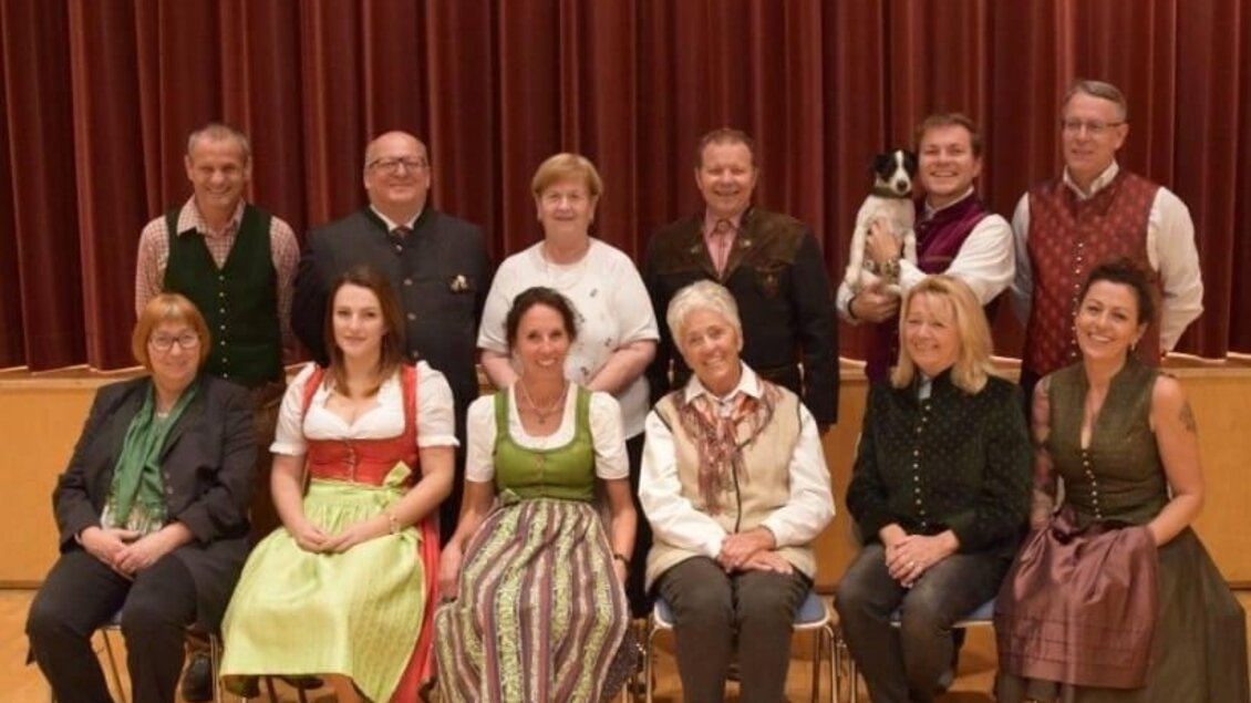 Eine Gruppe von Menschen in traditioneller Kleidung steht und sitzt auf Stühlen. Im Hintergrund ist ein roter Vorhang zu sehen. | © Murtaler Bauernbühne