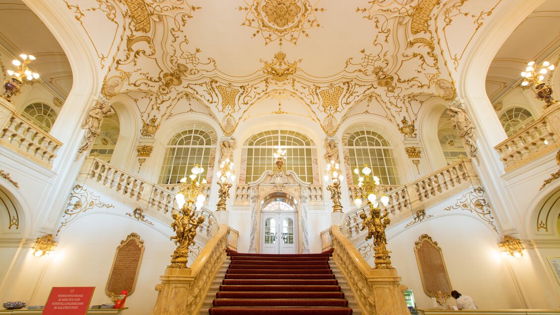 Ein prächtiger Eingangsbereich mit einer eleganten Treppe und aufwendigen Verzierungen. Das Licht von den Kronleuchtern schafft eine warme Atmosphäre. | © Graz Tourismus - Harry Schiffer