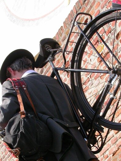 A musician in traditional clothing carries a wind instrument and a bag while walking through the streets of Graz on a bicycle. The musician is surrounded by a historic brick wall, which hints at the cultural atmosphere of a musical city stroll. | © STVLW