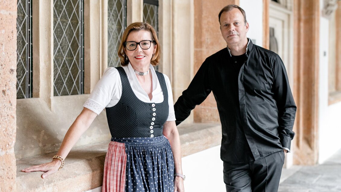 Ein Paar steht lächelnd an einer Mauer in einem historischen Gebäude. Die Frau trägt ein traditionelles Dirndl, während der Mann in schwarzer Kleidung gekleidet ist. | © Verein Neuberger Kulturtage