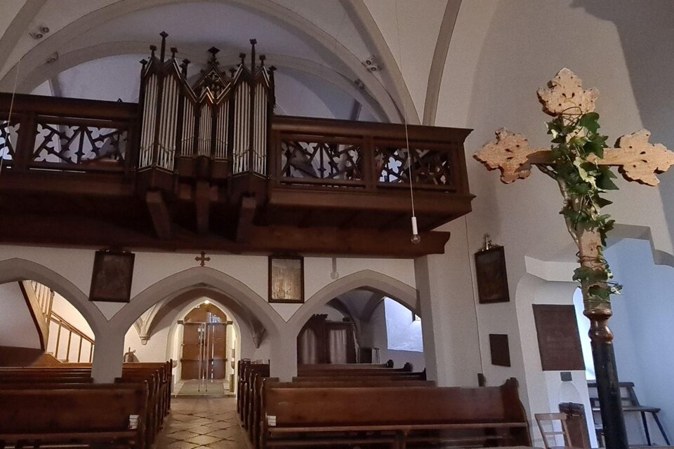 Eine Innenansicht einer Kirche mit einer Holzorgel und einem Kreuz im Vordergrund. Die Bänke sind aus Holz und die Wände sind hell gestrichen. | © Stephanie Bor