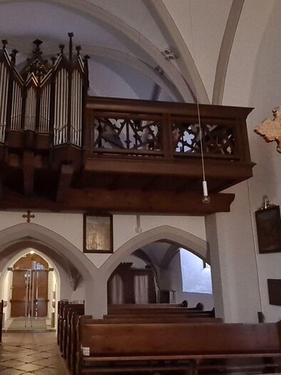 Eine Innenansicht einer Kirche mit einer Holzorgel und einem Kreuz im Vordergrund. Die Bänke sind aus Holz und die Wände sind hell gestrichen. | © Stephanie Bor