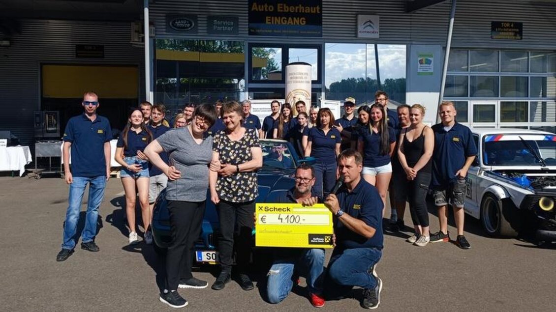 Eine Gruppe von Menschen steht vor einem Autohaus und hält einen großen Scheck über 4100 Euro. Im Hintergrund sind einige Autos und das Logos des Autohauses zu sehen. | © MSC Eberhaut/Martina Ertl