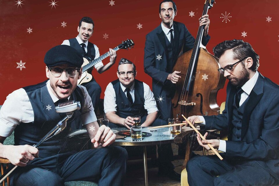 Eine Band mit fünf Musikern in eleganter Kleidung sitzt um einen Tisch. Der Hintergrund ist rot mit weißen Schneeflocken. | © Marija-Kanizaj