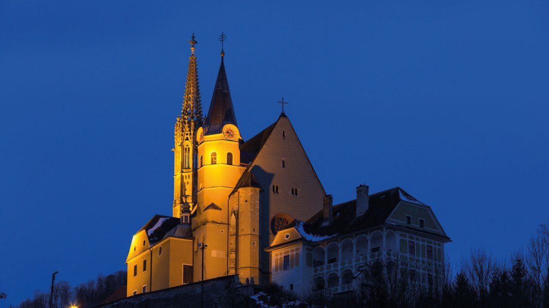 Eine beeindruckende Kirche erleuchtet in der Dämmerung. Der Himmel ist tiefblau und die Architektur ist hoch und markant. | © Region Graz-Harry Schiffer