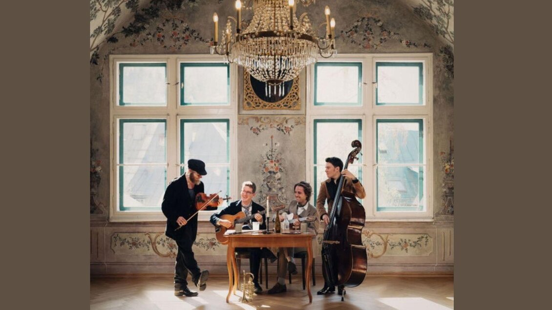 Eine musikalische Gruppe spielt in einem eleganten Raum mit einem Kronleuchter. Sie sitzen an einem Tisch und haben verschiedene Instrumente dabei. | © Kammerhofmuseum